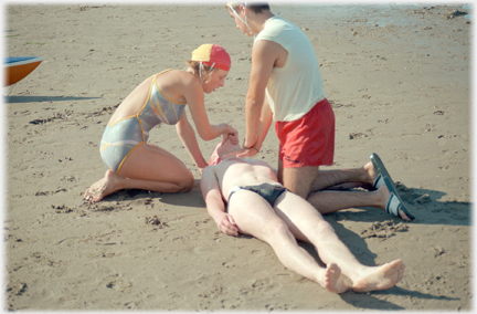 Two life savers kneeling and demonstrating CPR with casulty between them.