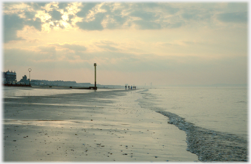 View of beach with low water, family in distance and complex hazy light from half obscured sun.