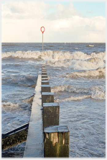 Wooden groin with waves crashing around it.