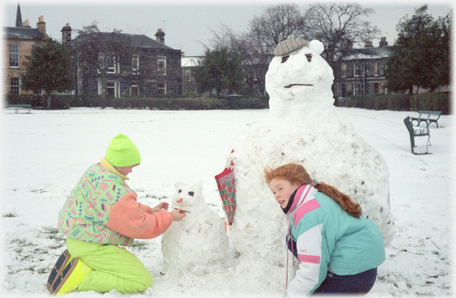 Snowmen with two children building them.