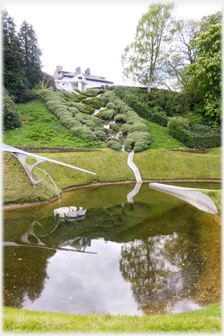 White stepped zig-zag cascade covered in shrubs with pond in foreground.