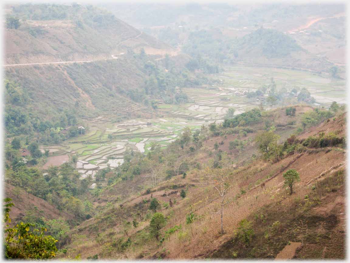 Misted view from hill looking down onto green fields on valley floor.