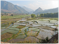 Fertile valley floor with scores of fields separated by small embankments and mountains in the background.