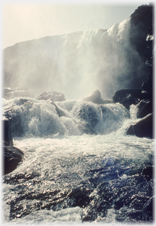 Water cascading over a cliff edge into a river with spray filling the air.