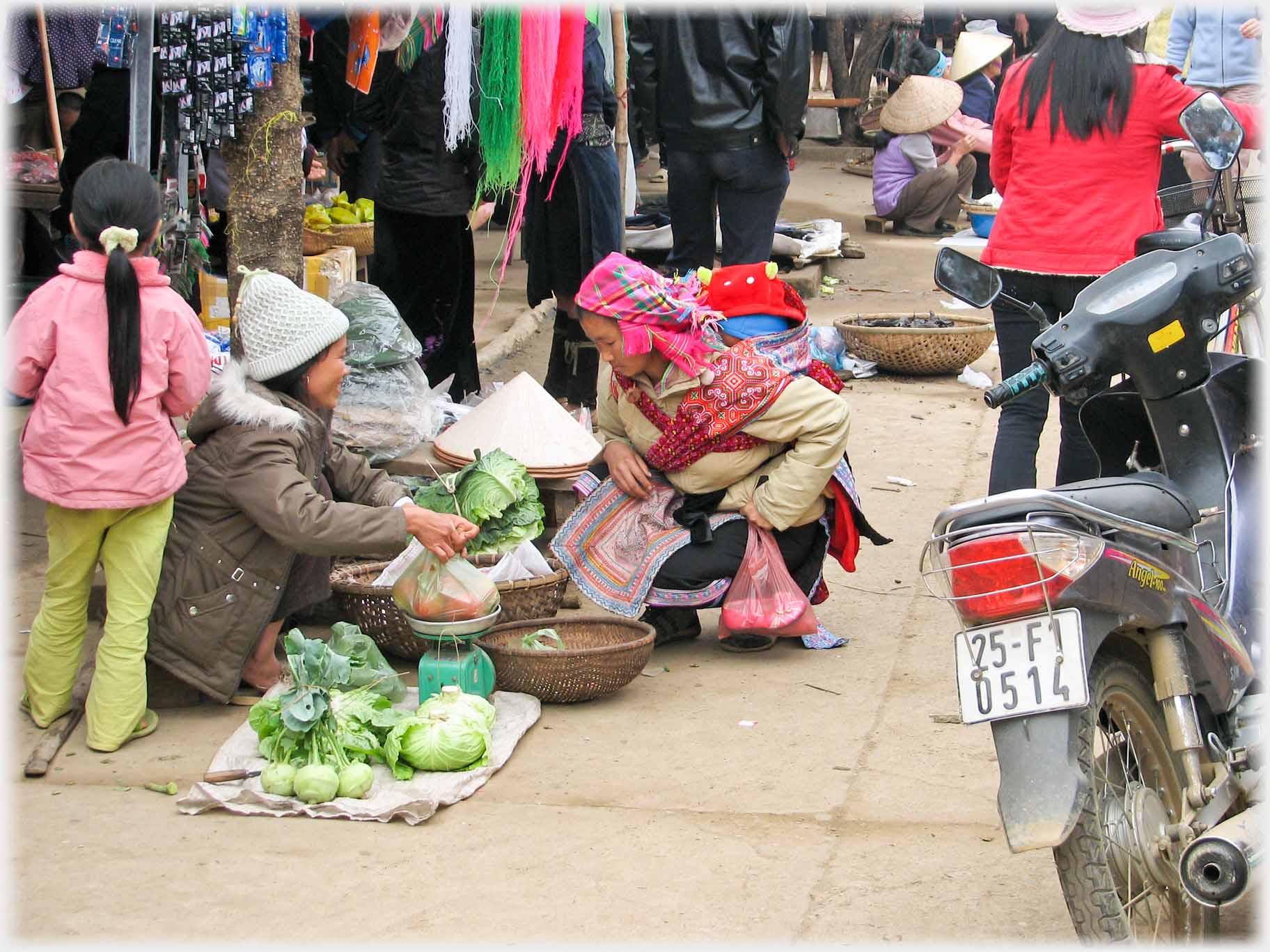 Vendor wraping goods for customer squatting on pavement.