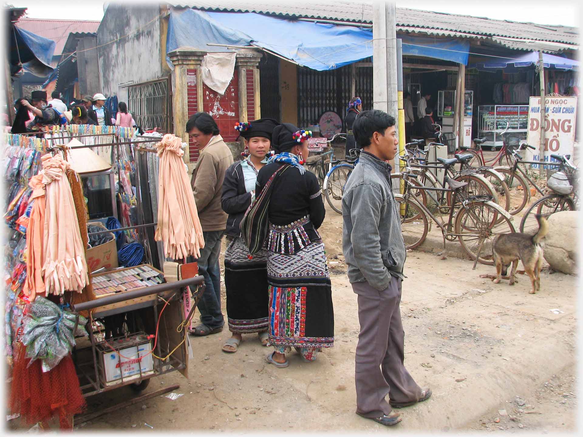 Heavily loaded hidden hand-cart, two women standing, man standing looking at range of parked bicycles.