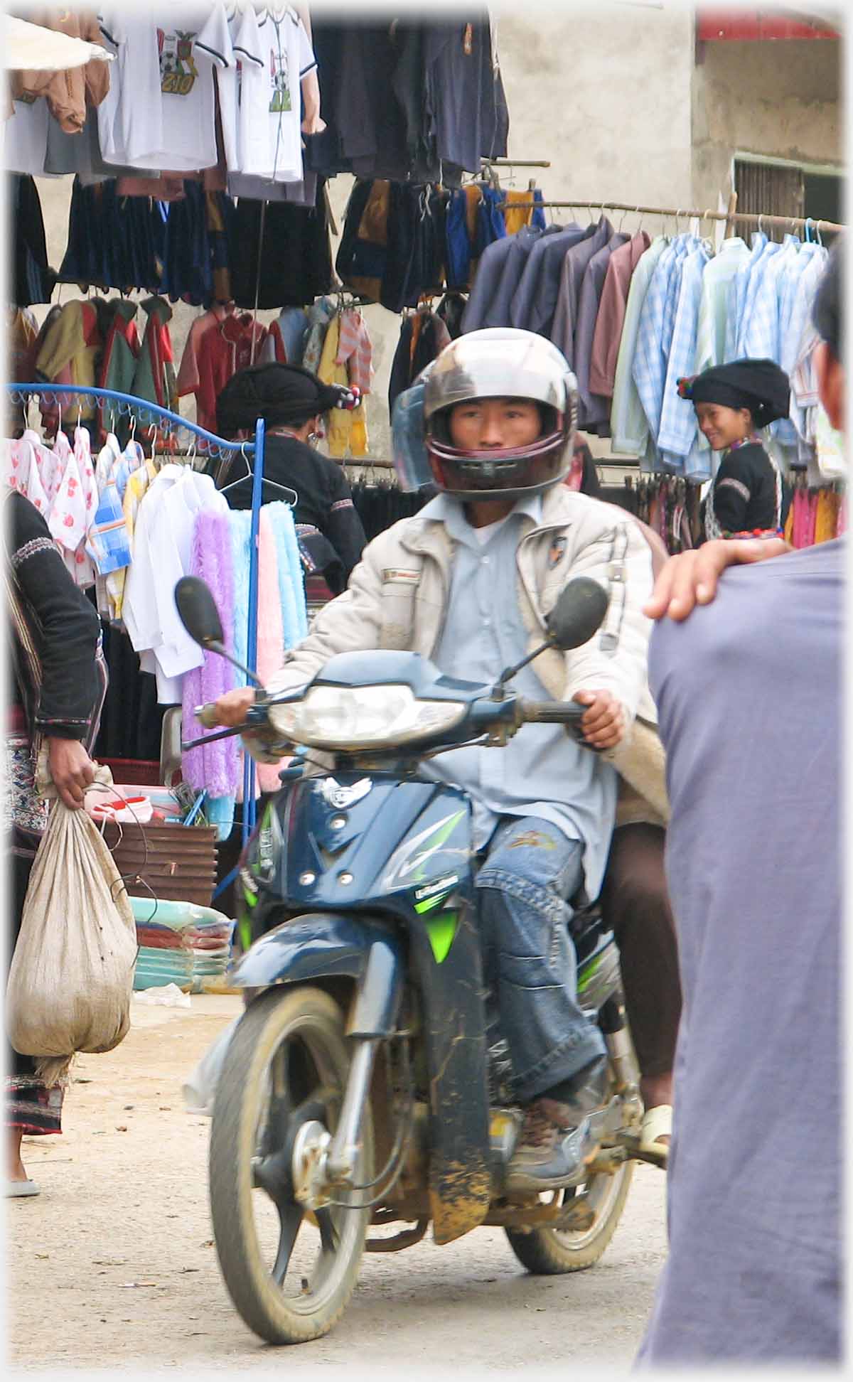 Man on motorbike riding past stalls.
