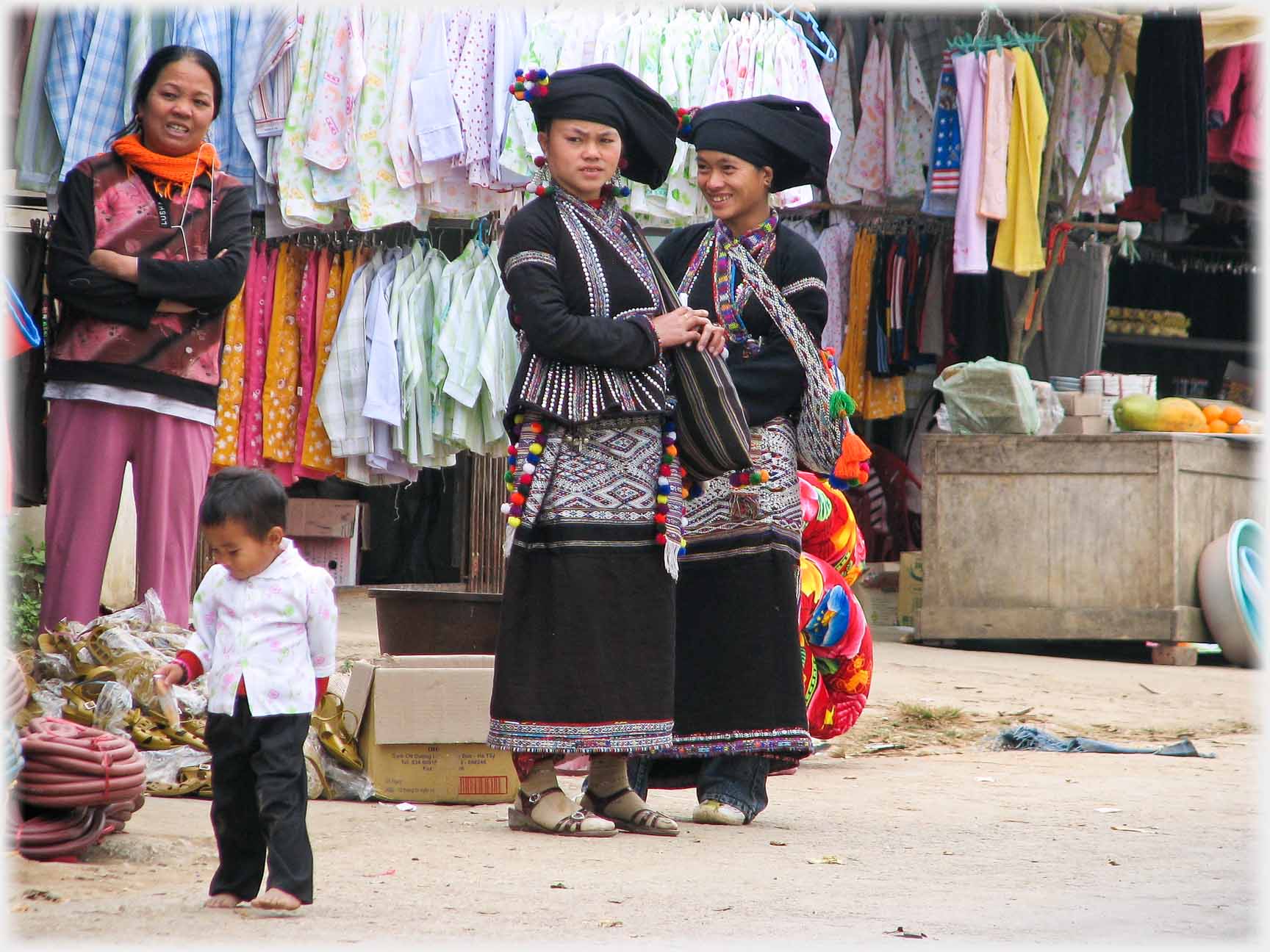 Two women in black, stall holder and small child.