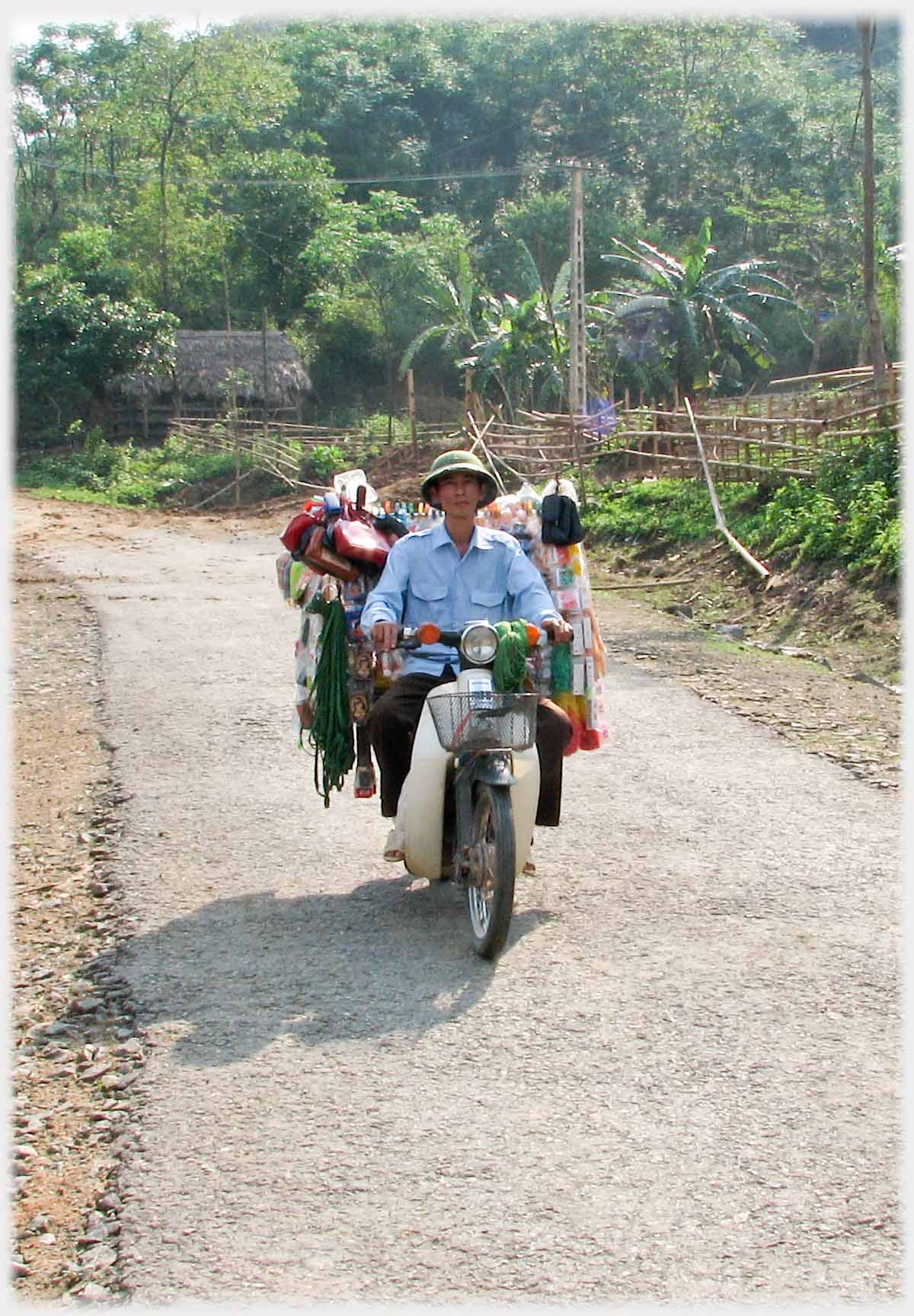 Motorbike approaching with high array of goods behind driver.