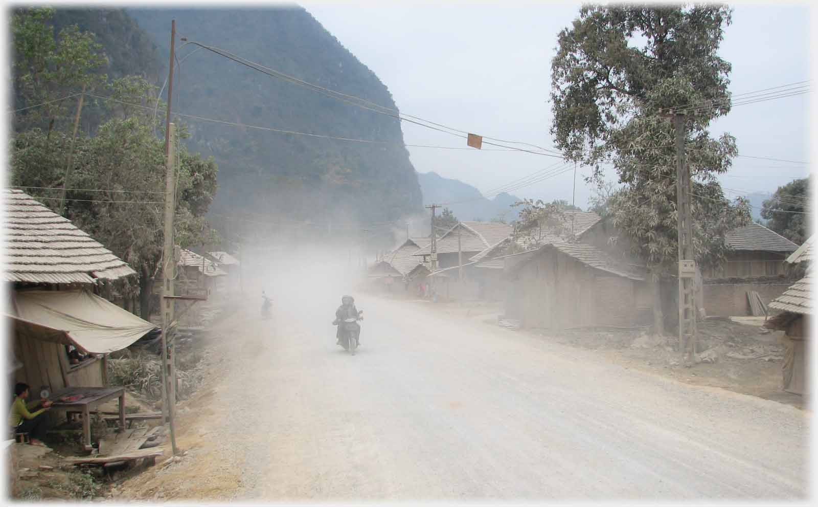 Motorbike appearing out of dust on road.