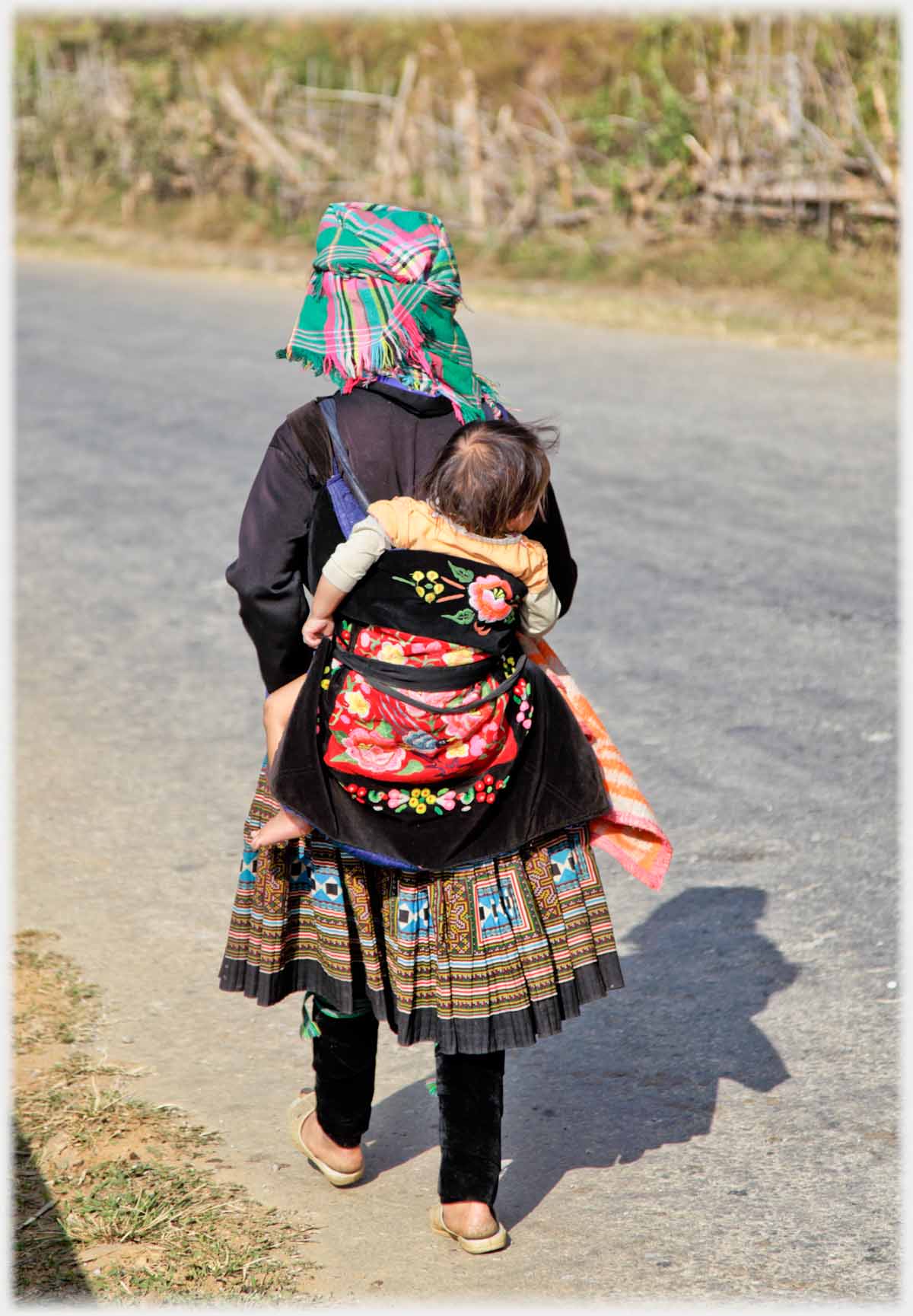 Woman walking on road with baby in bag on her back.