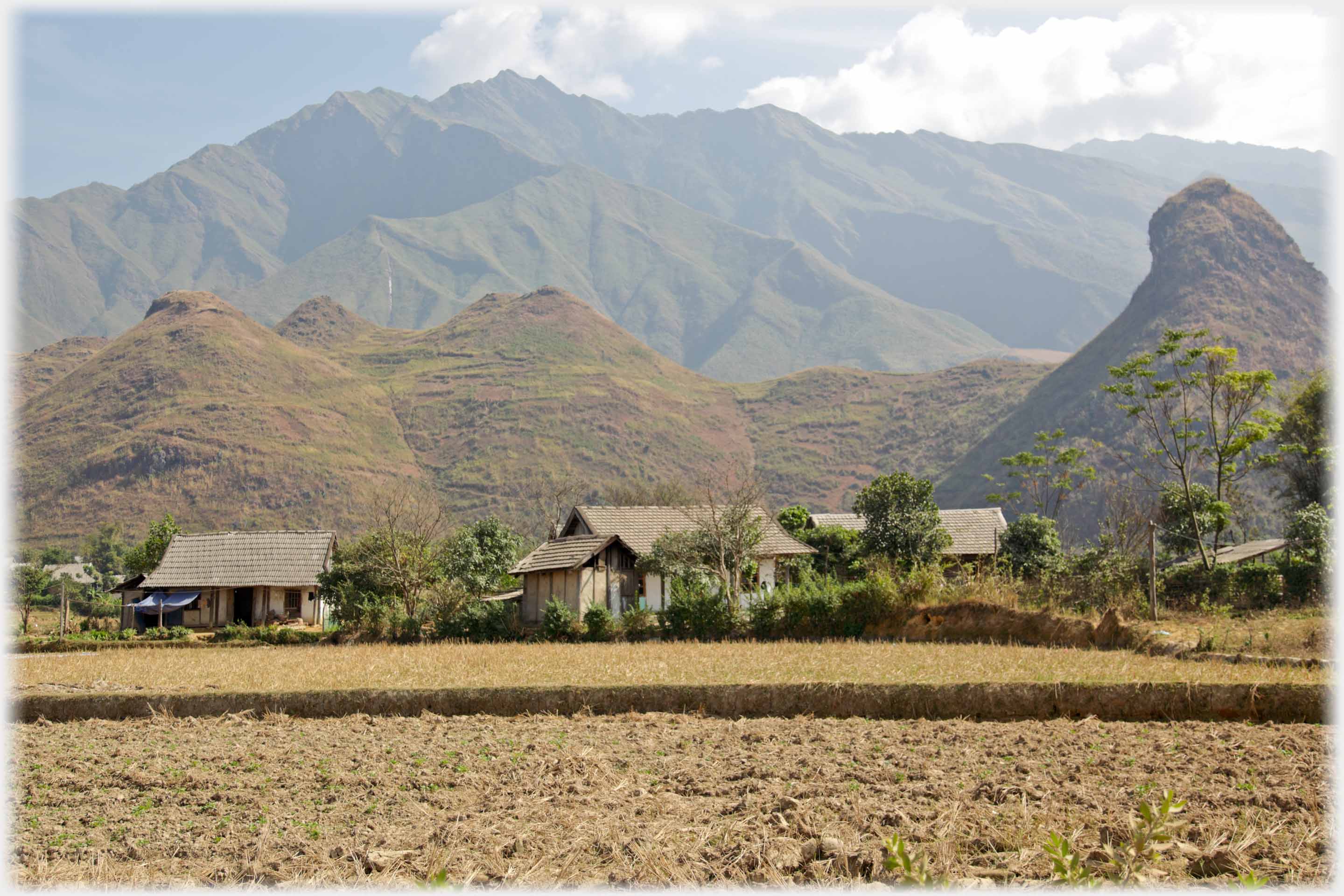 Small plain houses with close hills, one angular, mountains beyond.