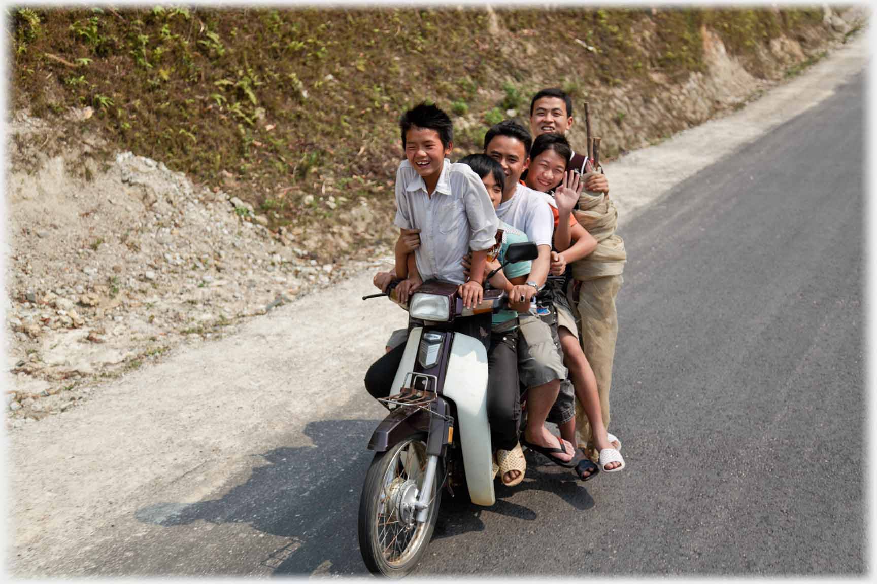 Facing motorbike, five heads can be seen and five feet, but six left hands.