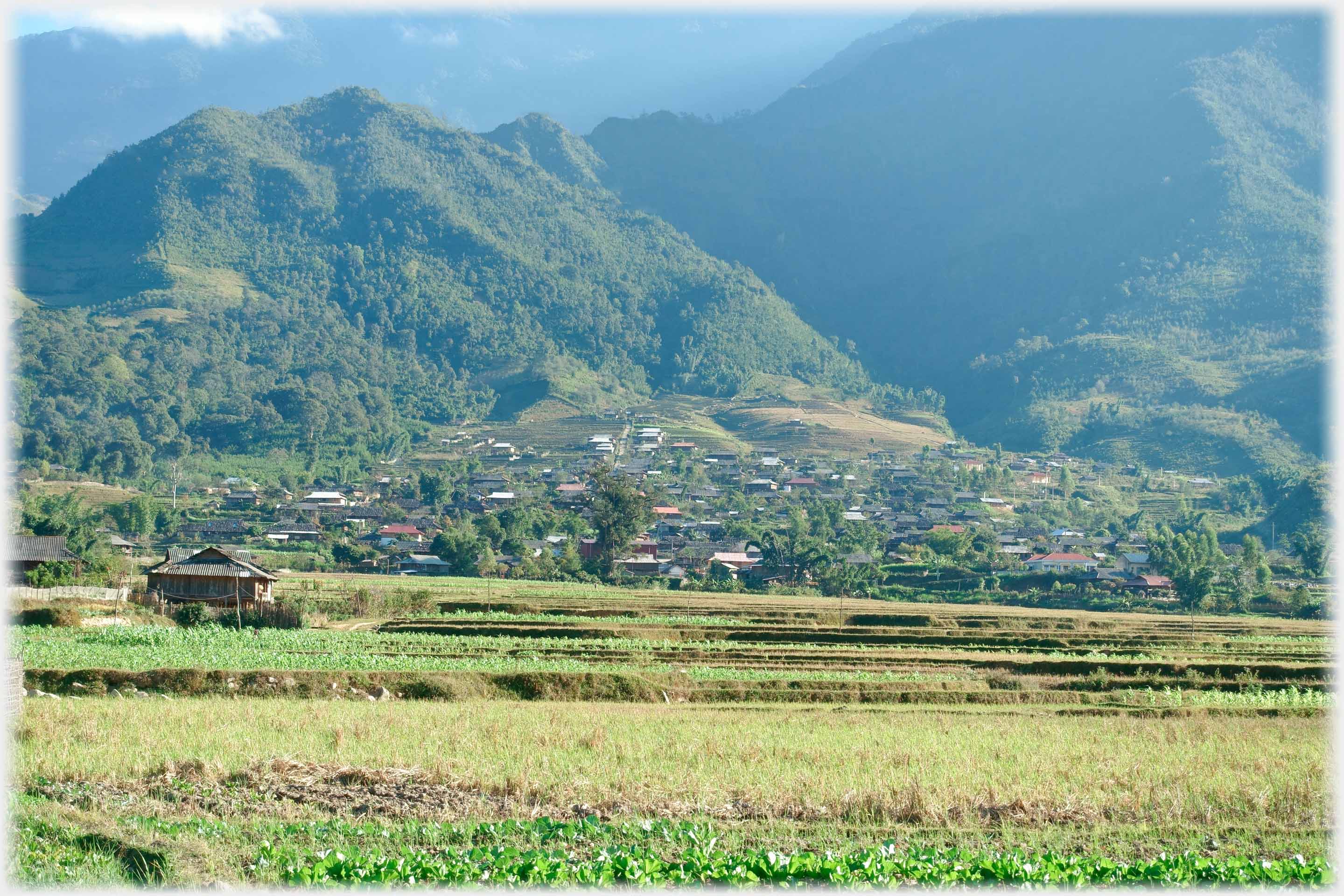 High wooded mountains with village at their foot and fields in foreground.