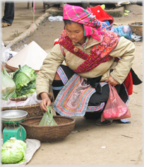 Woman in colourful garb squatting examing produce in a basket.