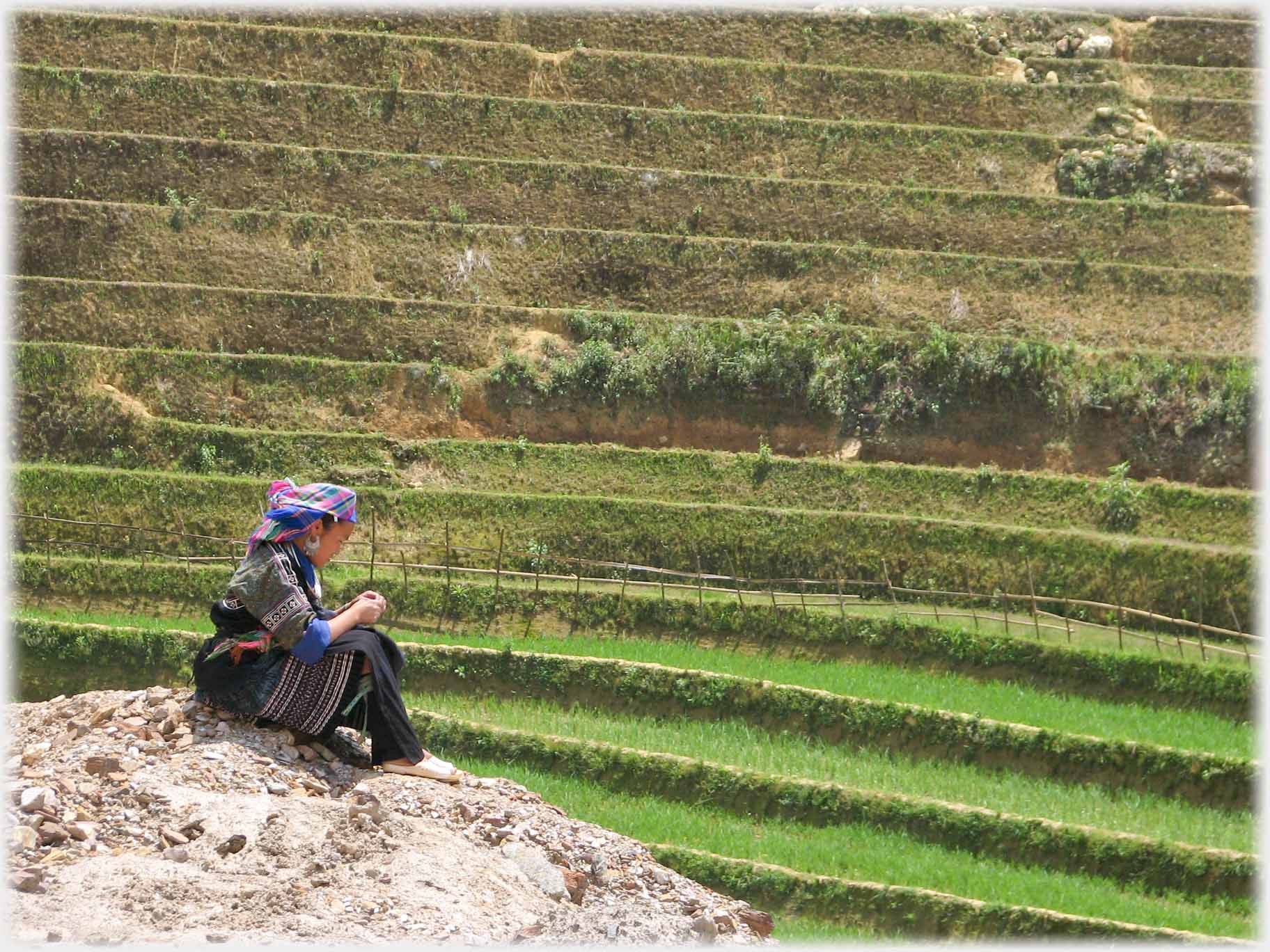 Woman sitting on ground looking at hands, terracing behind.