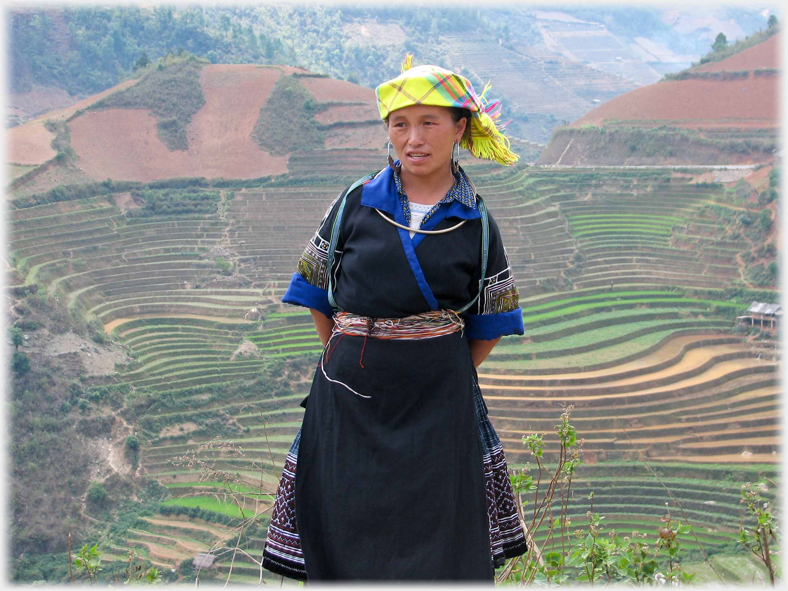 Woman standing with extensive terraced hillsides behind her.