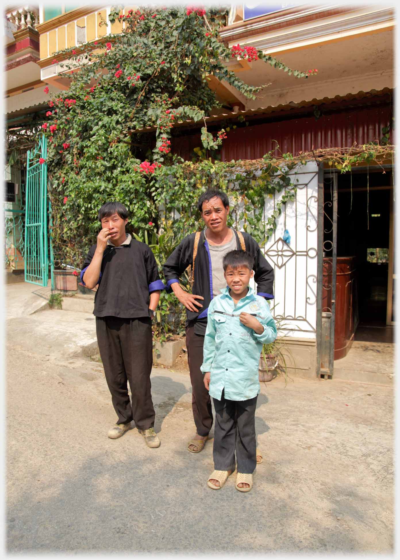 Two men and a boy outside town houses, faces screwed up as they look at camera.