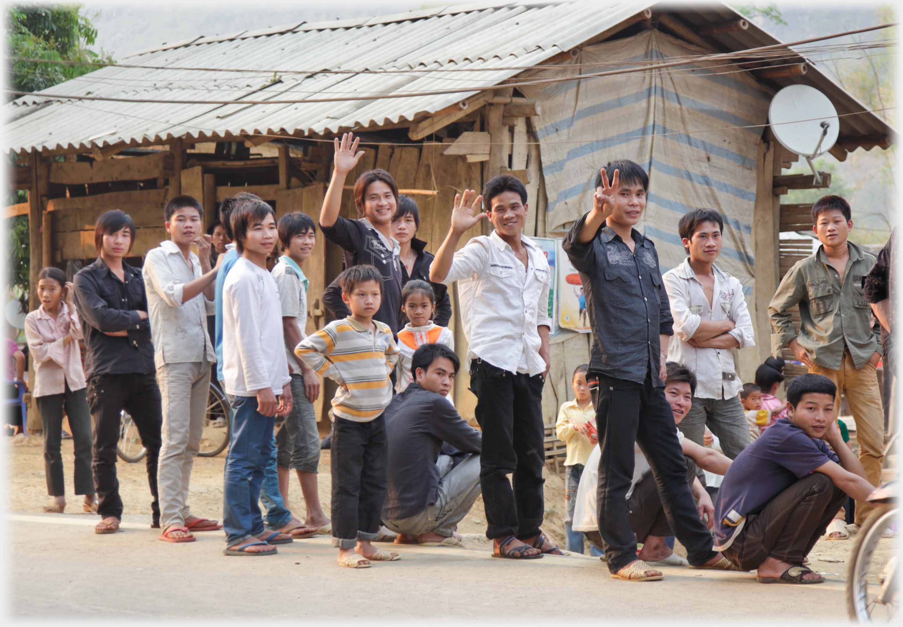 Group of young men standing and waving and squatting and looking - one unsure.