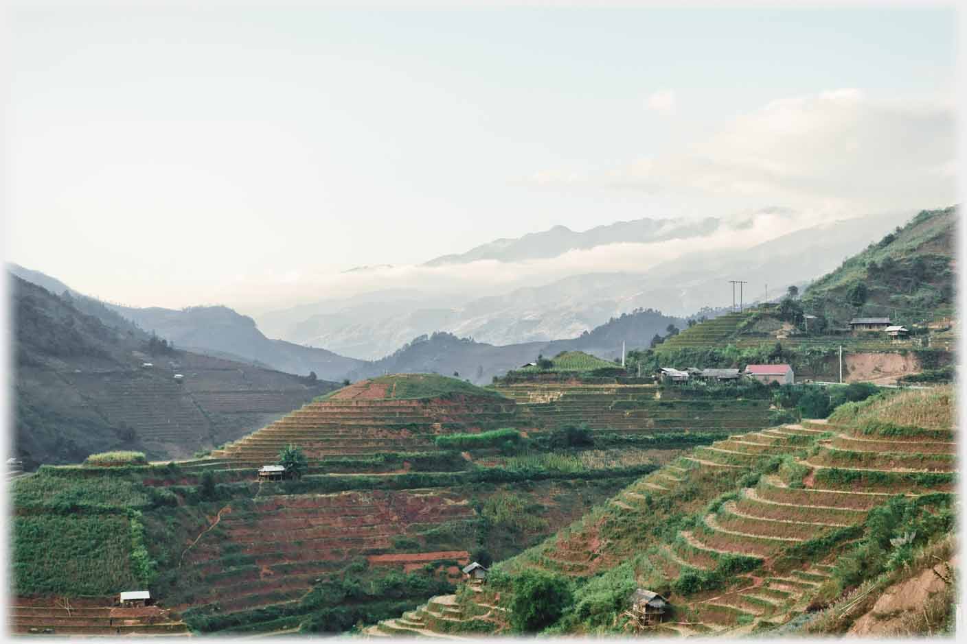 Valley with clouded mountains in the distance, village to right and terraces decending.