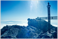 A cross amongst rocks with clouds below.