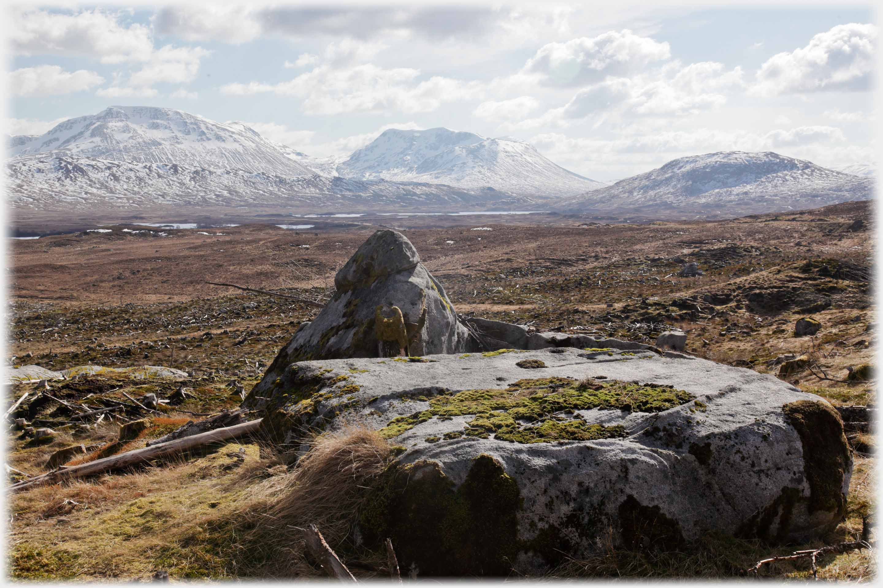 Distinct flat and conical rocks in foreground, moorland and soft distant hills .