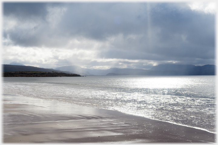 Sun playing through dark clouds and onto the sea and sand.