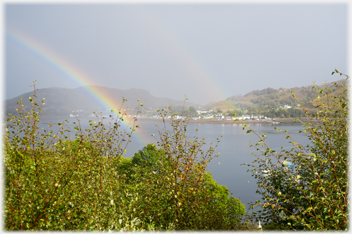 Looking across bay to village at woters edge, rainbow and its echo falling on the water.