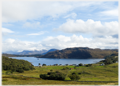 Row of houses at loch side with hills beyond.