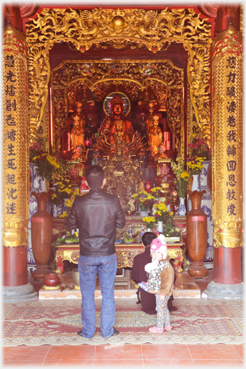 Extremely elaborate gilt and red main altar with two people and child in front of it.