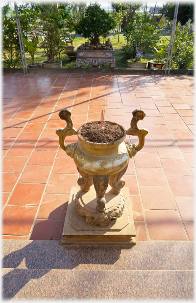 Plain cloured urn for incense sticks with courtyard behind.