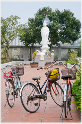 Three bicycles parked in the courtyard with Buddha statue beyond.