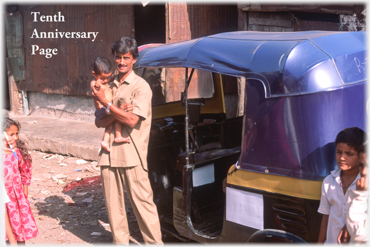 Man standing beside auto holding baby.