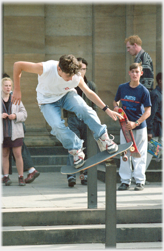 Skateboarder in air being watched by others.