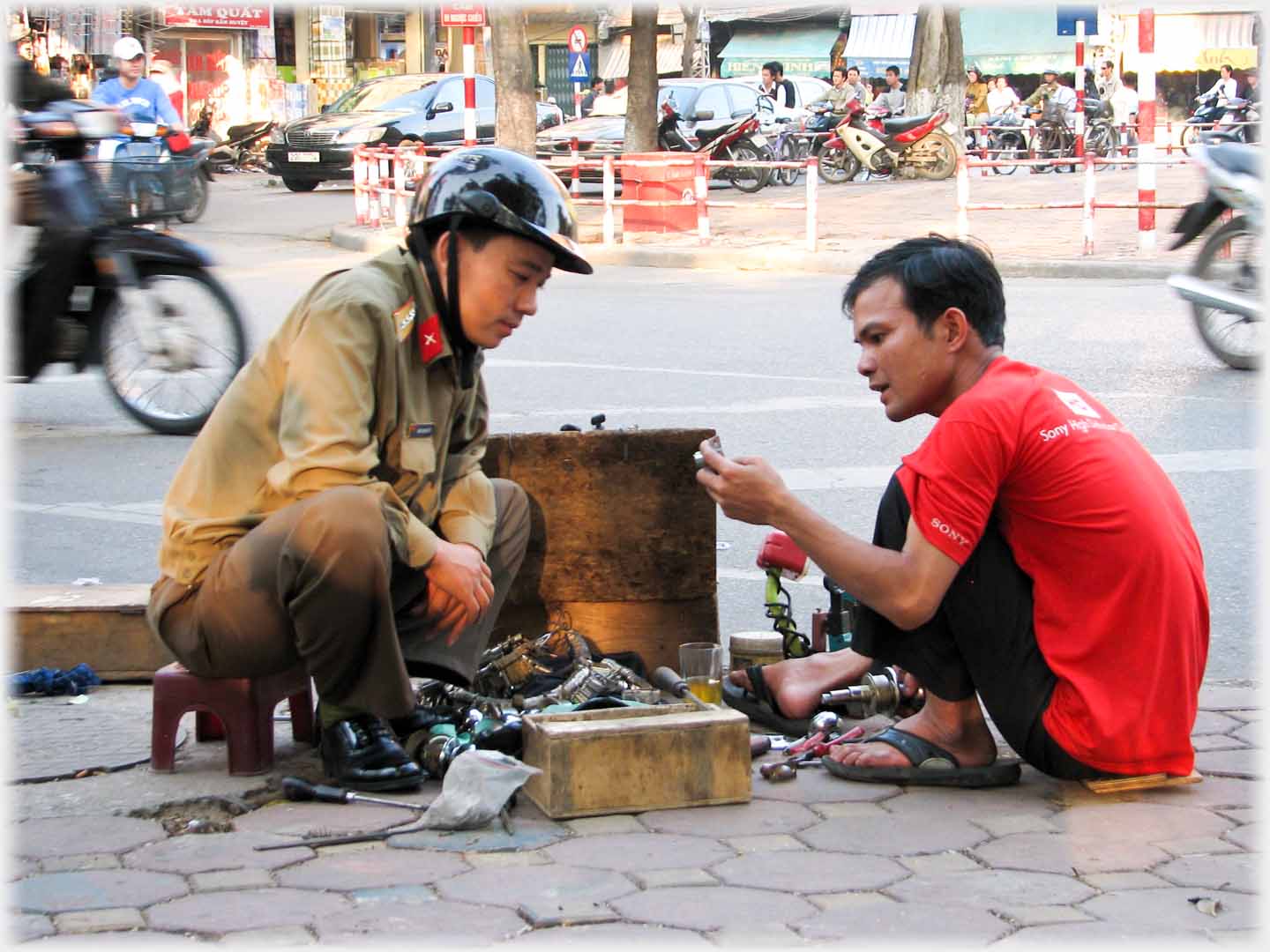 Two men sqatting by road looking a metal objects from box.