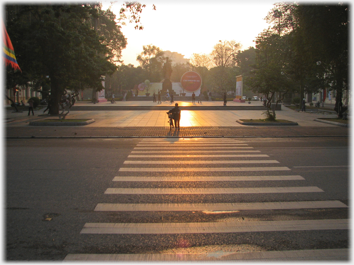 Low sun across sqare and zebra crossing on road.