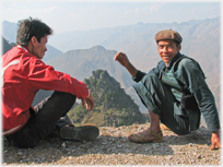 Two men squatting with mountains behind.