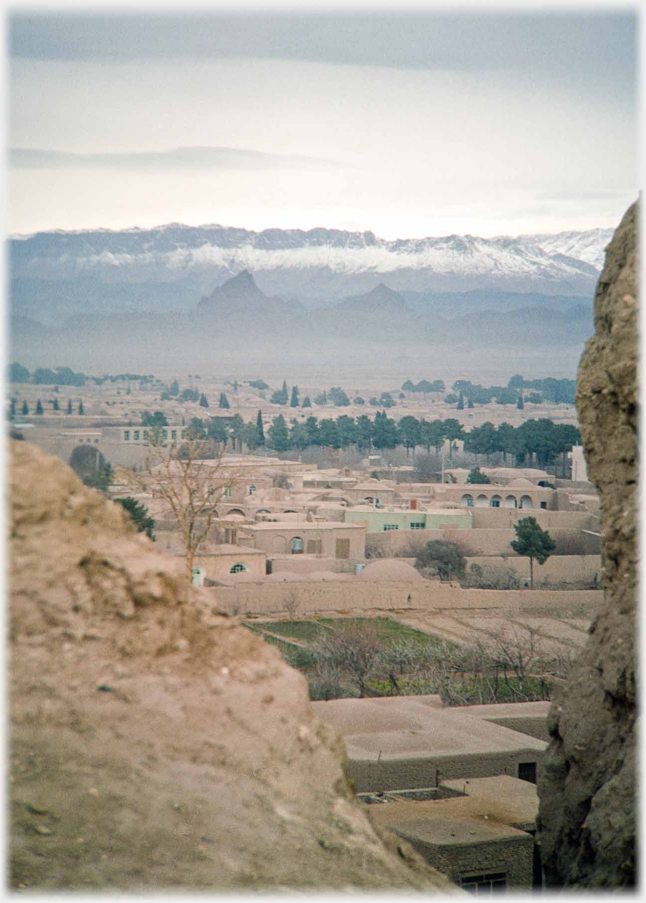 Looking out between rocks across a mud house city towards mountains.