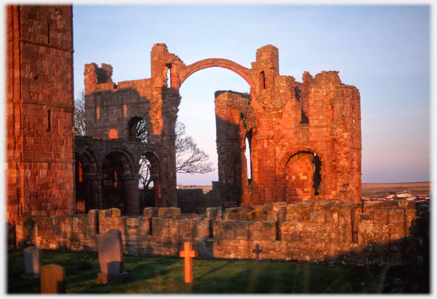 Ruin with high arch and cross caught in sunset.
