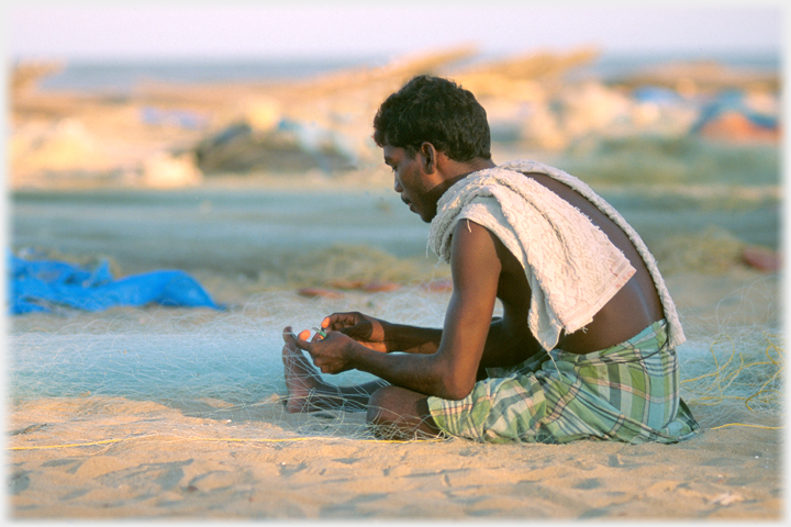 Man sitting on sands mending nets.