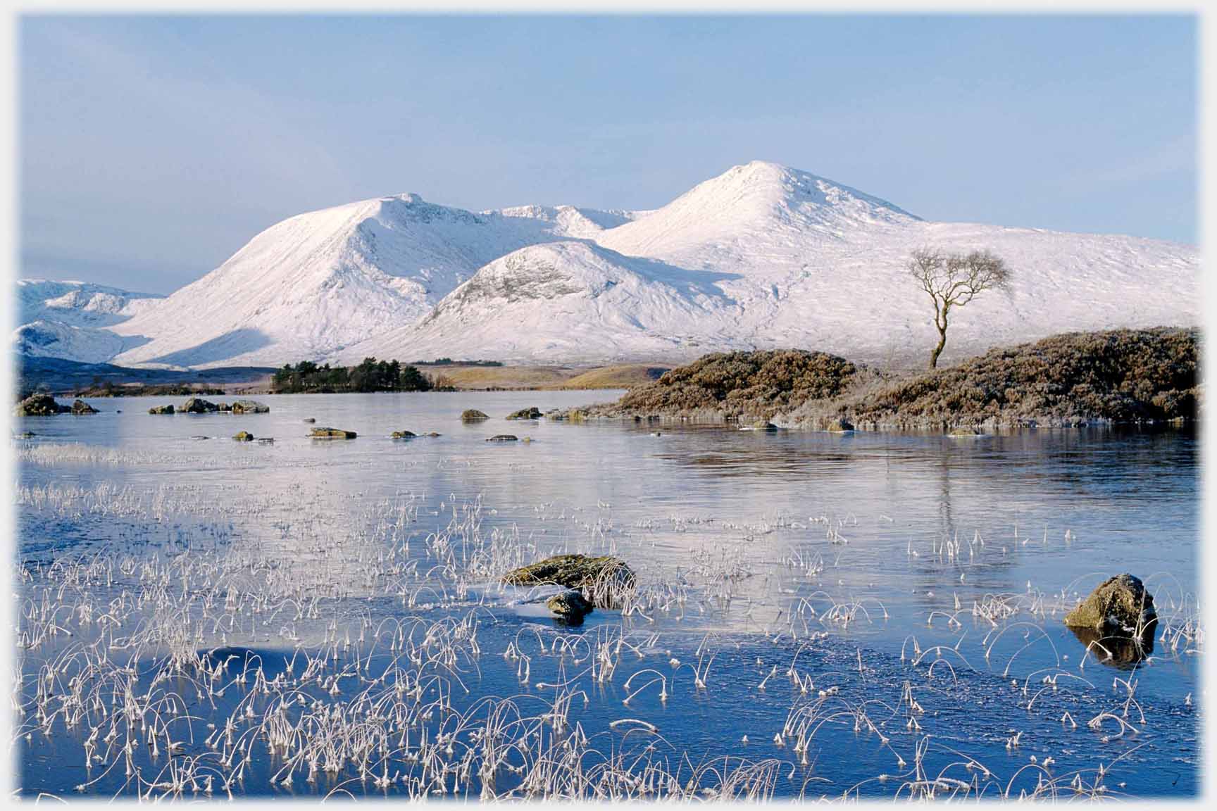 Snow covered hills with frozen loch in foreground.