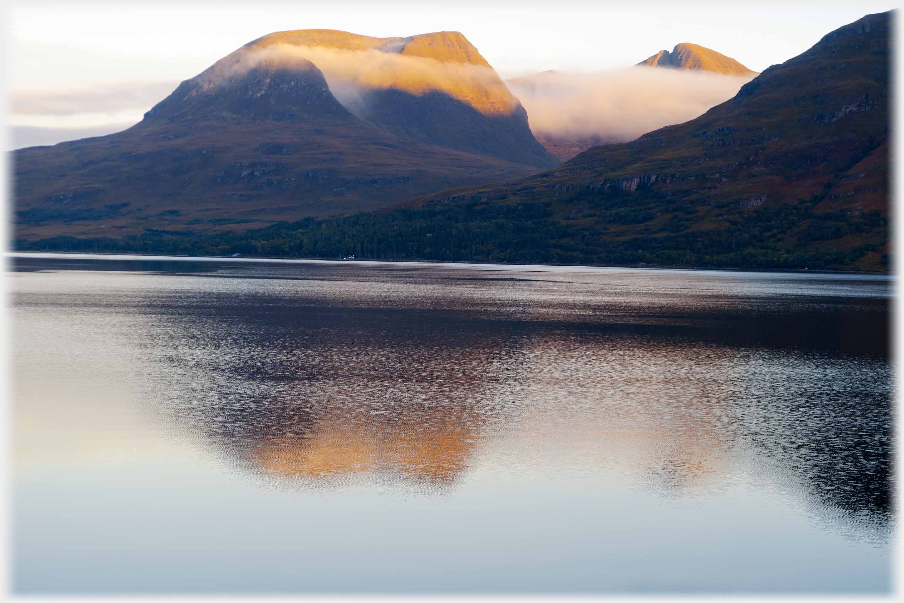 Mountains reflected in sea with clouds around them.