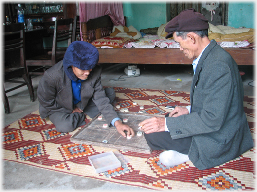 Two older men playing Chinese Chess on a mat.