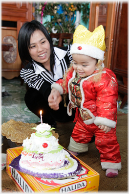 Mother and infant by cake with candle.