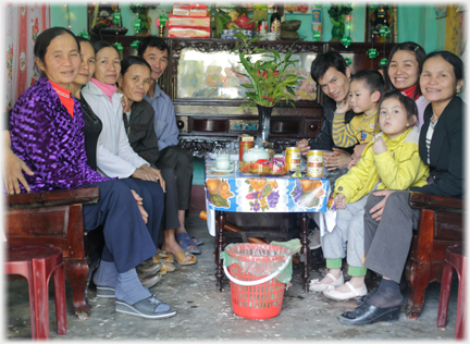 Eight adults plus children cram benches beside a table, display cabinet behind.