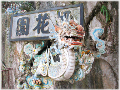 A sharp toothed dragon on a wall with a Chinese sign behind it.
