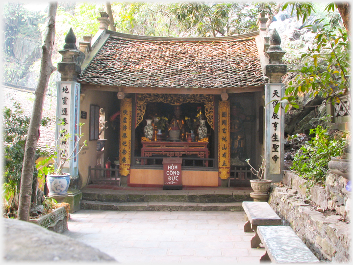 Small shrine with tiled roof and large notice on box.