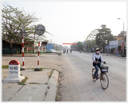 Schoolgirl on bike near mile post, empty road beyond her.