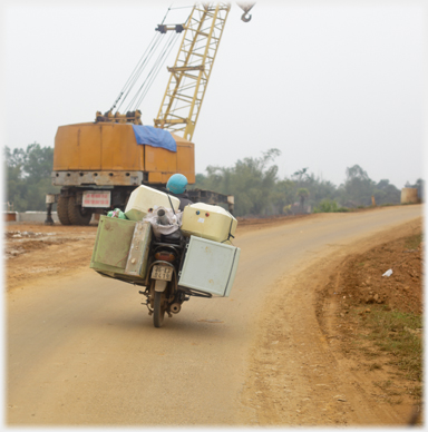 Motorcycle with fridge strapped to one side and washing machine to the other, water tank and sink on top.