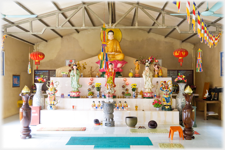 A four tiered altar with many statues and ritual objects, overhead metal frame of the roof.